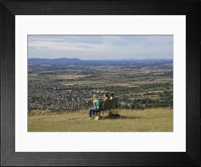 Framed Print : Three girls sitting on bench looking at the view over Bishops Cleeve village Framed Print : Three girls sitting on bench looking at the view over Bishops Cleeve village