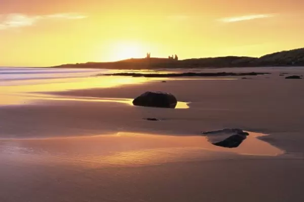 View along Embleton Bay at sunrise, with silhouette of Dunstanburgh Castle in the distance