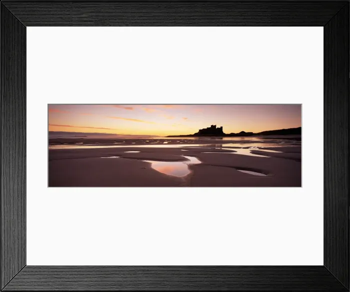 Framed Print : Bamburgh castle in silhouette at sunrise, with rock pools on empty beach Framed Print : Bamburgh castle in silhouette at sunrise, with rock pools on empty beach