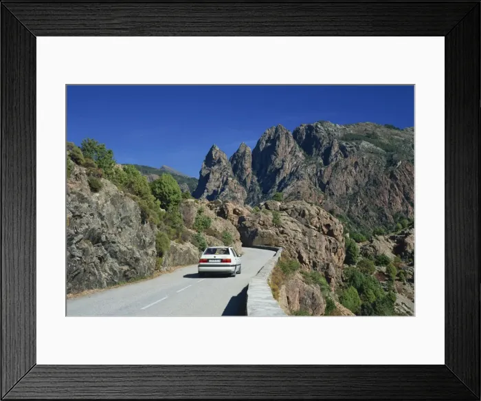 Framed Print : Car on mountain road above the Spelunca Gorge, with Capo Ferolata behind Framed Print : Car on mountain road above the Spelunca Gorge, with Capo Ferolata behind