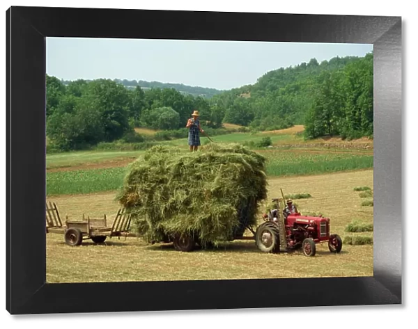 Farming couple with tractor and full trailer during haymaking in a field near Lalbenque