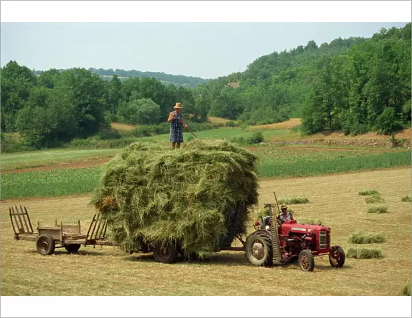 Farming couple with tractor and full trailer during haymaking in a field near Lalbenque