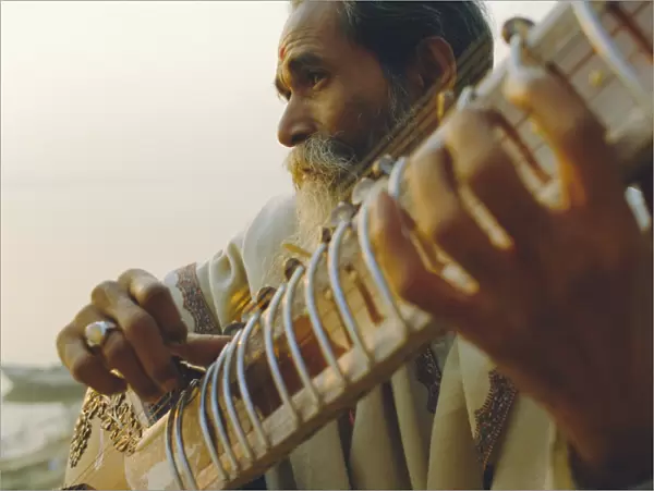 Elderly man playing the sitar beside the Ganges (Ganga) River