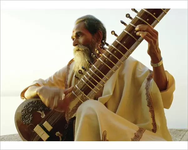 Elderly man playing a sitar by the Ganges (Ganga) River