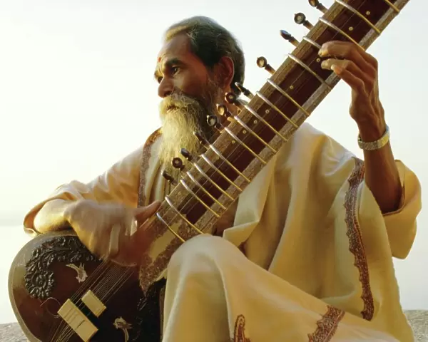 Elderly man playing a sitar by the Ganges (Ganga) River