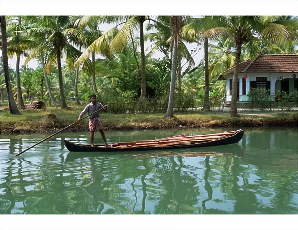 Man with pole pushing boat forwards on a Kerala backwater