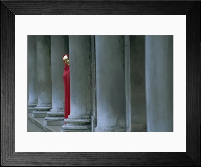 Framed Print : Carnival model in red cape and gold mask peering from columns in St Framed Print : Carnival model in red cape and gold mask peering from columns in St