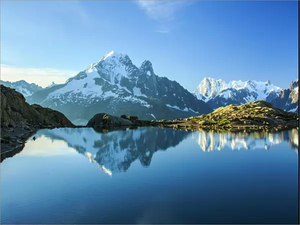 The snowy peaks of Mont Blanc are reflected in the blue water of Lac Blanc at dawn
