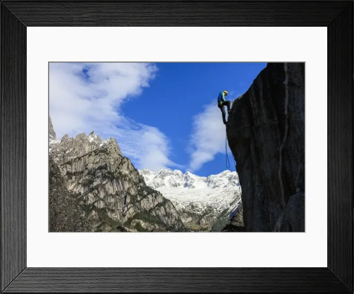 Framed Print : Climber on steep rock face in the background blue sky and snowy peaks of the Alps Framed Print : Climber on steep rock face in the background blue sky and snowy peaks of the Alps