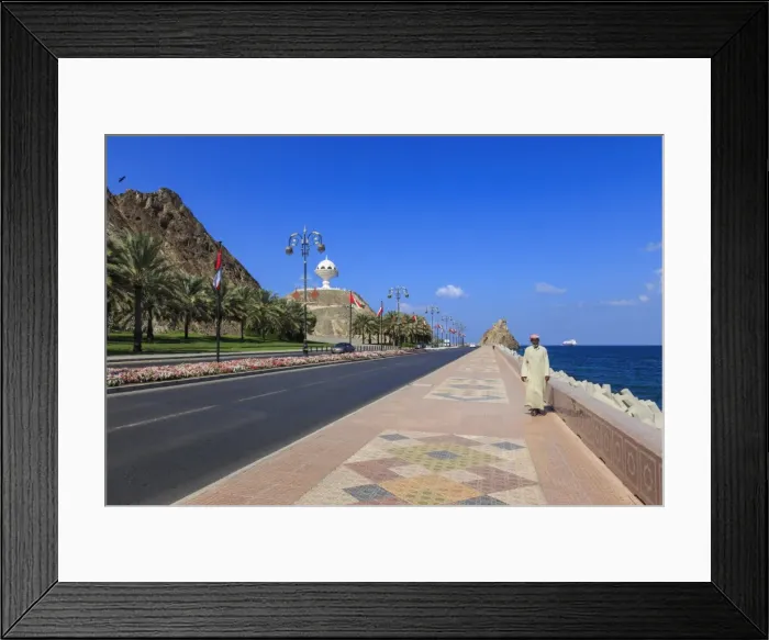 Framed Print : Man wearing dishdasha walks along Mutrah Corniche with national flags, flower beds Framed Print : Man wearing dishdasha walks along Mutrah Corniche with national flags, flower beds