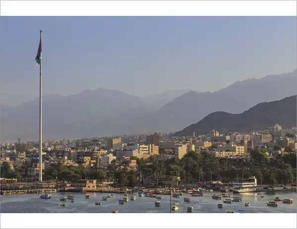 Elevated view of Aqaba seafront with huge Jordanian flag, boats and hazy mountains in distance