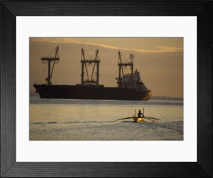 Framed Print : Figure silhouetted at dusk in an outrigger canoe near huge cargo ship Framed Print : Figure silhouetted at dusk in an outrigger canoe near huge cargo ship