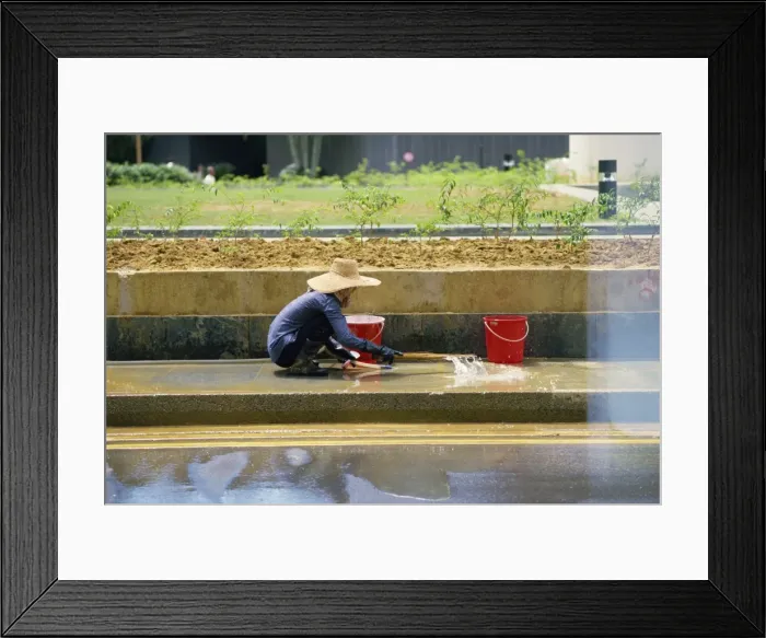 Framed Print : An elderly woman in a straw hat washes the pavement Framed Print : An elderly woman in a straw hat washes the pavement