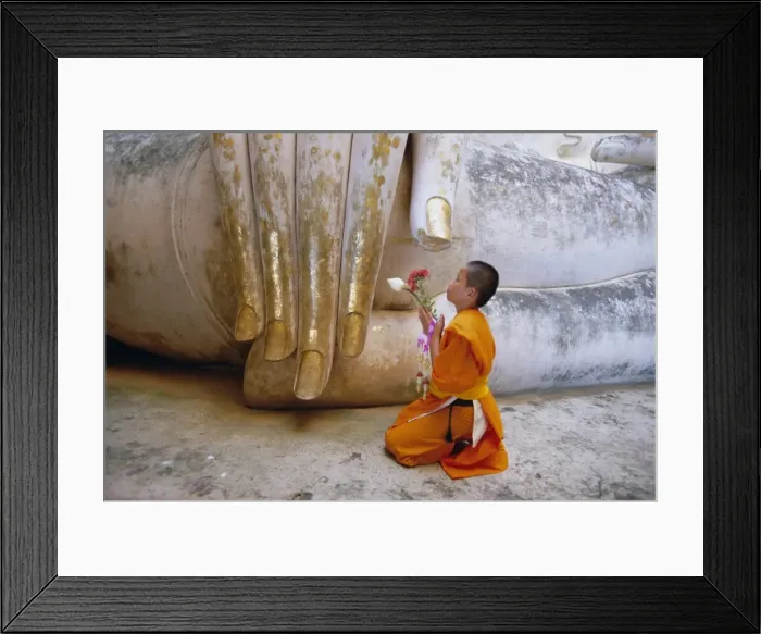 Framed Print : Novice Buddhist monk kneeling beneath the Phra Atchana Buddha statue