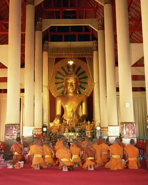 Monks in saffron robes kneel before a statue of the