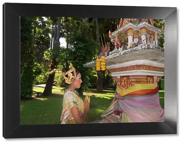 Girl in traditional Thai clothes praying at a spirit house
