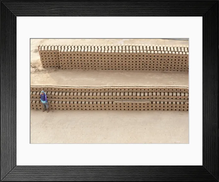 Framed Print : Female brick worker standing beside hand made bricks stacked to dry before baking Framed Print : Female brick worker standing beside hand made bricks stacked to dry before baking