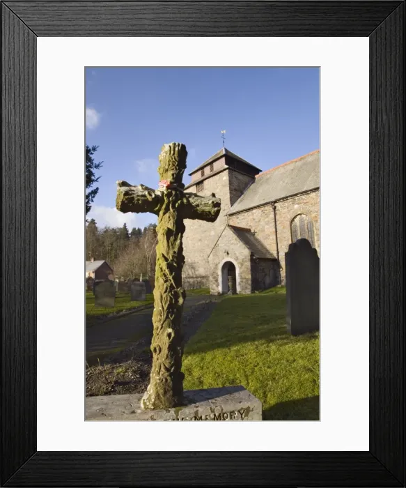 Framed Print : Carved stone cross headstone in front of the 14th century St Framed Print : Carved stone cross headstone in front of the 14th century St