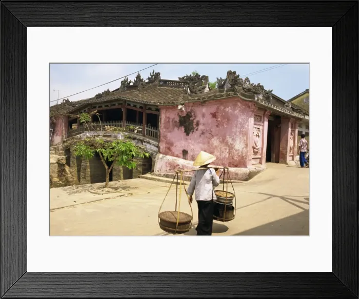 Framed Print : Woman carrying baskets on a pole by a covered bridge