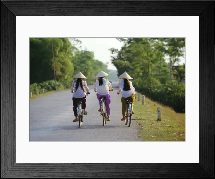 Framed Print : Three girls in conical hats cycling on rural road north of Hanoi Framed Print : Three girls in conical hats cycling on rural road north of Hanoi