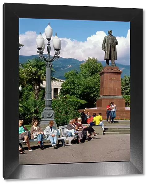 People sitting on benches near a statue of Lenin in Yalta