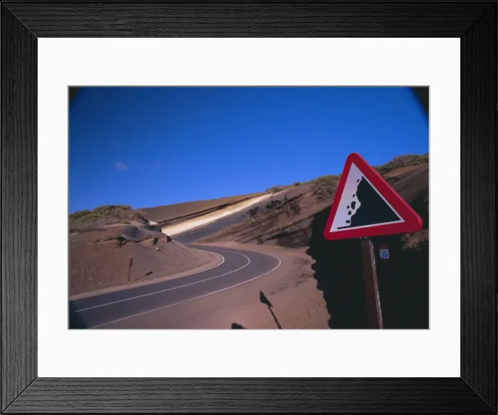 Framed Print : Sign on a road with volcanic stratified rocks in the background Framed Print : Sign on a road with volcanic stratified rocks in the background