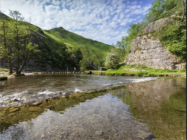 Dovedale reflections, hikers on stepping stones and Thorpe Cloud, limestone gorge in spring