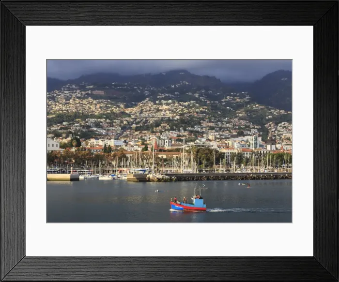 Framed Print : Funchal town from sea with fishing boat, lit by evening sun with foggy mountain backdrop Framed Print : Funchal town from sea with fishing boat, lit by evening sun with foggy mountain backdrop