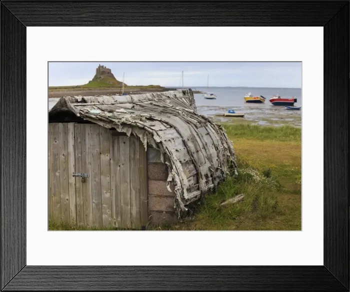 Framed Print : Upturned weathered boat hut with Lindisfarne Castle and fishing boats at low tide Framed Print : Upturned weathered boat hut with Lindisfarne Castle and fishing boats at low tide