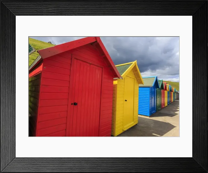 Framed Print : Row of colourful beach huts and their shadows, with grassy cliffs, West Cliff Beach Framed Print : Row of colourful beach huts and their shadows, with grassy cliffs, West Cliff Beach