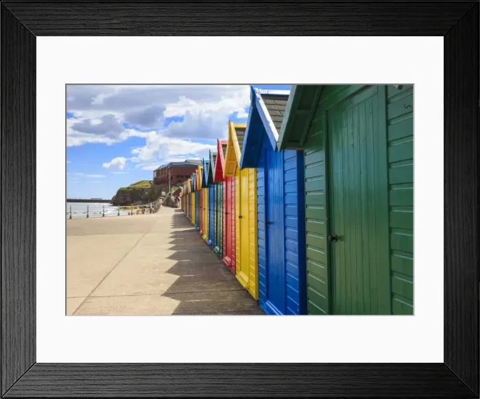 Framed Print : Row of colourful beach huts and their shadows, distant surfers in sea, West Cliff Beach Framed Print : Row of colourful beach huts and their shadows, distant surfers in sea, West Cliff Beach