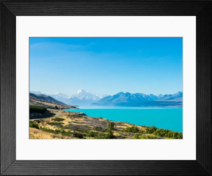 Framed Print : A road winds along the edge of a turquoise blue lake with mountains in the distance Framed Print : A road winds along the edge of a turquoise blue lake with mountains in the distance