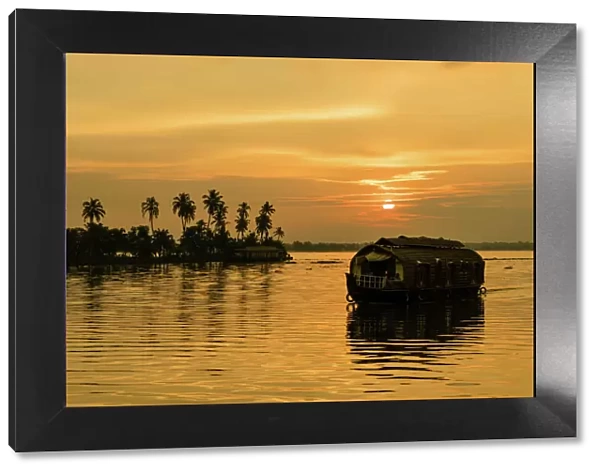 A traditional houseboat moves past the setting sun on the Kerala Backwaters, Kerala