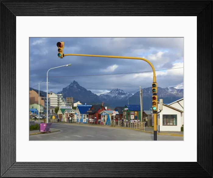 Framed Print : Colourful houses on touristic road framed by traffic lights post with snowy mountain chain beyond Framed Print : Colourful houses on touristic road framed by traffic lights post with snowy mountain chain beyond