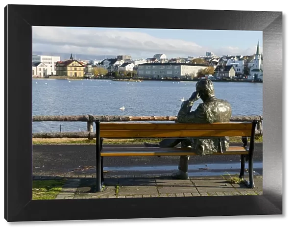 Sculpture of a man sitting on a park bench in front of Tjornin Lake and the Historic
