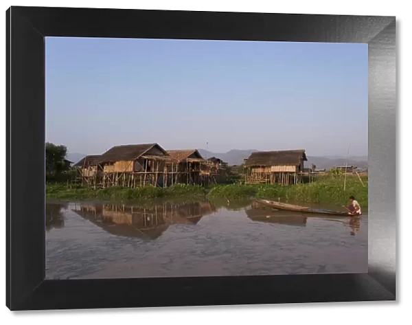 A man paddles his canoe past one of the floating villages on Inle Lake, Myanmar (Burma)