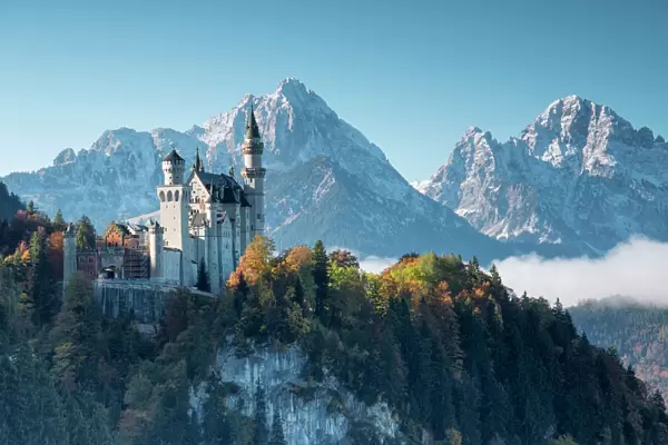 Neuschwanstein Castle surrounded by colorful woods and snowy peaks, Fussen, Bavaria