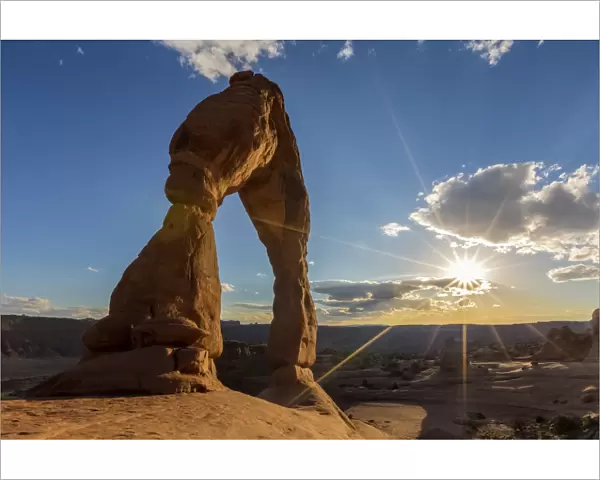 Delicate Arch with sun and clouds at golden hour, Arches National Park, Moab, Grand County