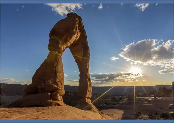 Delicate Arch with sun and clouds at golden hour, Arches National Park, Moab, Grand County
