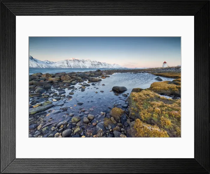 Framed Print : Grass and rocks frame the lighthouse surrounded by frozen sea and snowy peaks at dawn Framed Print : Grass and rocks frame the lighthouse surrounded by frozen sea and snowy peaks at dawn