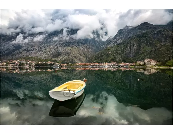 A small fishing boat sits in the reflection of the Old Town (stari grad) of Kotor in Kotor Bay