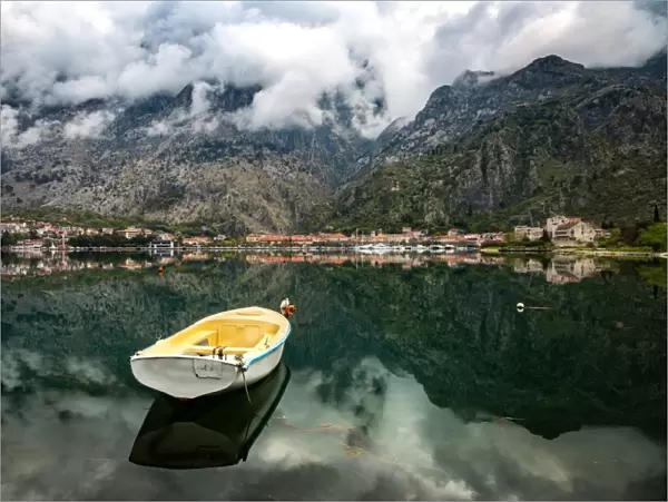 A small fishing boat sits in the reflection of the Old Town (stari grad) of Kotor in Kotor Bay