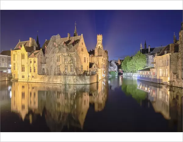 The medieval Belfry and historic buildings reflected in Rozenhoedkaai canal at night