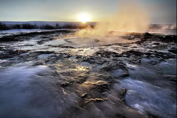 Hot pools and steam from Strokkur Geysir at sunrise, winter, at geothermal area beside