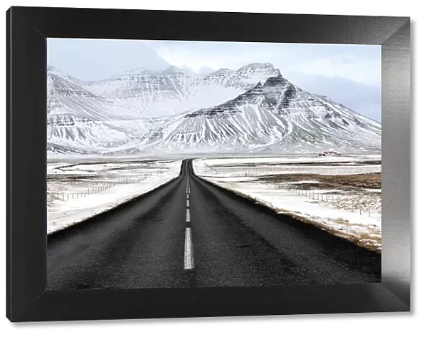 Black tarmac road leading towards snow covered mountains in winter, South Iceland