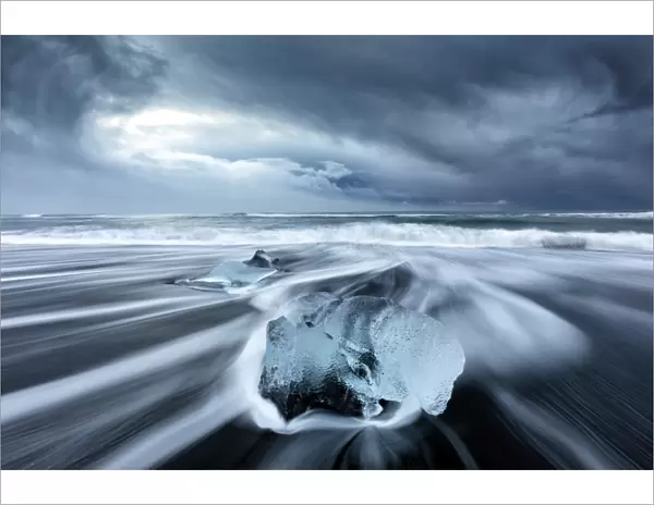 Glacier ice on black sand beach with waves washing up the beach on a stormy winter day