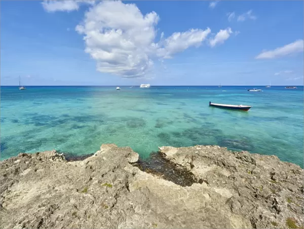 Rocky coastline in Cayman Islands with fishing boat in the transparent blue water