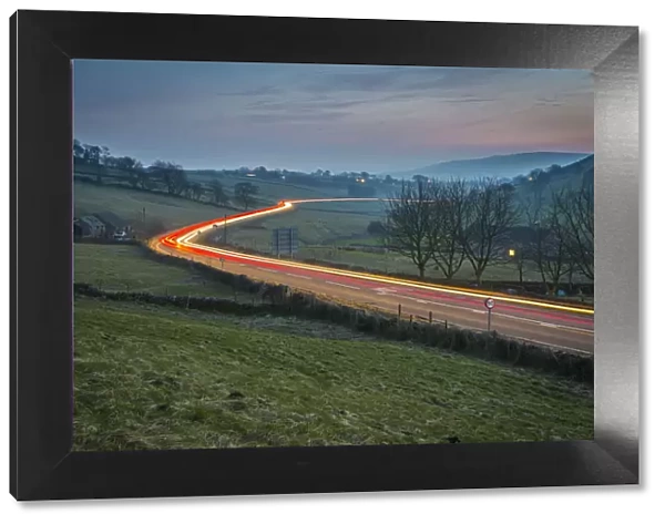 View of vehicle trail lights on A623 at Sparrowpit at dusk, Peak District National Park
