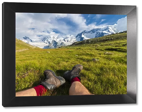 Hiker rests on grass looking towards Monte Rosa massif, Riffelalp, Zermatt, canton of Valais