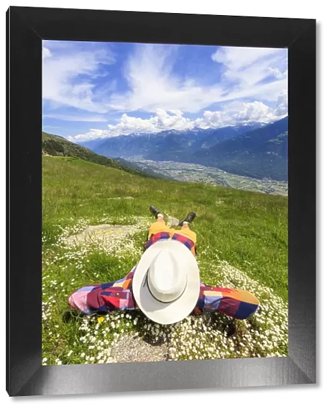 Rear view of man with hat lying on grass, Alpe Bassetta, Valtellina, Sondrio, Lombardy